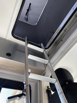 Interior of an RV rental: A silver ladder provides access to an upper sleeping bunk, with a roof hatch and storage units.