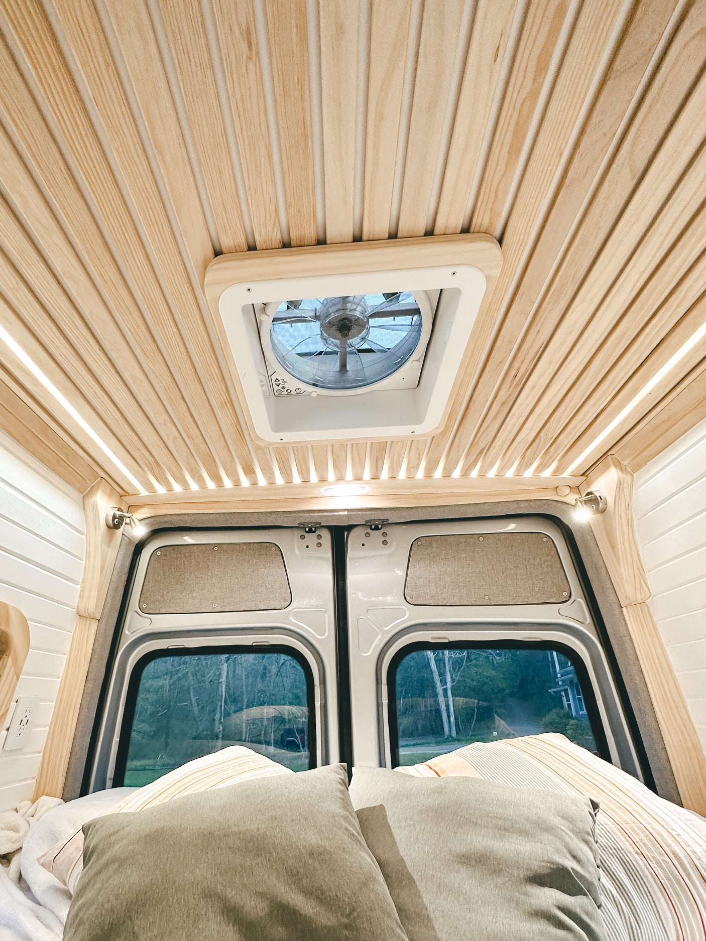 Cozy rv rental interior with a slatted wooden ceiling, roof fan, and inviting bed by the rear windows.