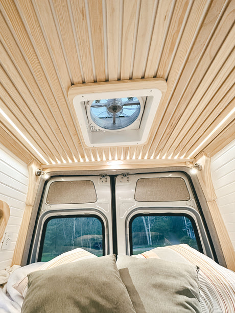 Cozy rv rental interior with a slatted wooden ceiling, roof fan, and inviting bed by the rear windows.