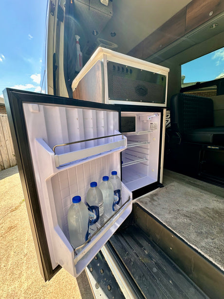RV rental interior: open fridge with water bottles, a control panel, and seating in a well-equipped camper van.