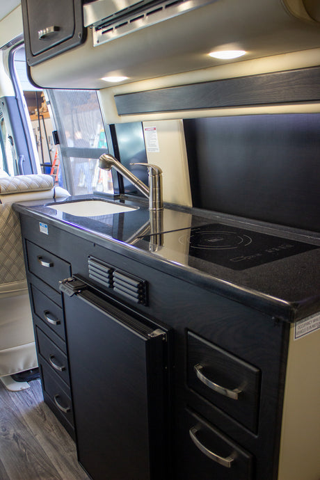 Compact RV rental kitchen featuring a sink, induction stove, fridge, and dark cabinetry.