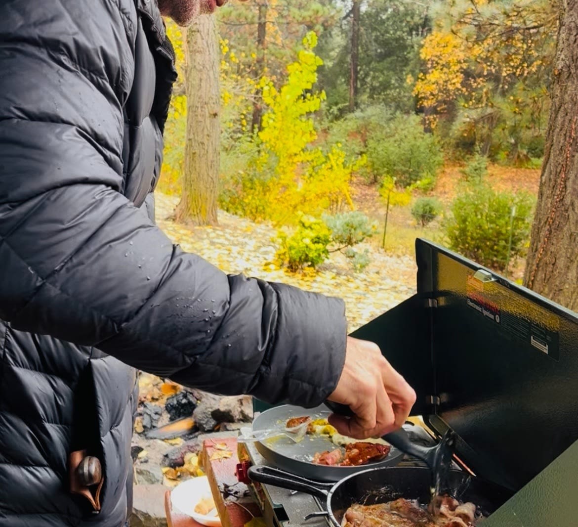  parked amidst yellow leaves under trees for your next adventure.|A unique rv rental experience: a rooftop tent deployed over a black teardrop camper trailer at a campsite.|A person cooking bacon & eggs outdoors on a portable stove amidst autumn foliage. Perfect for your RV rental adventure!|A wild turkey roams past an RV rental campsite — photo 6