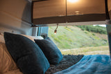 Cozy RV rental interior with a comfortable bed, overhead cabinets, and a scenic nature view from the window.
