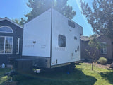 Modern white Elusive Trailers LO PRO CABIN, an off-grid solar-powered RV rental, parked on a sunny lawn.