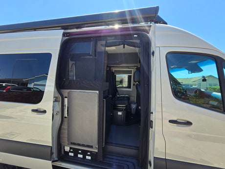 This RV rental's open side door reveals a compact interior with a sink, fridge, and seating, ready for mobile adventures.