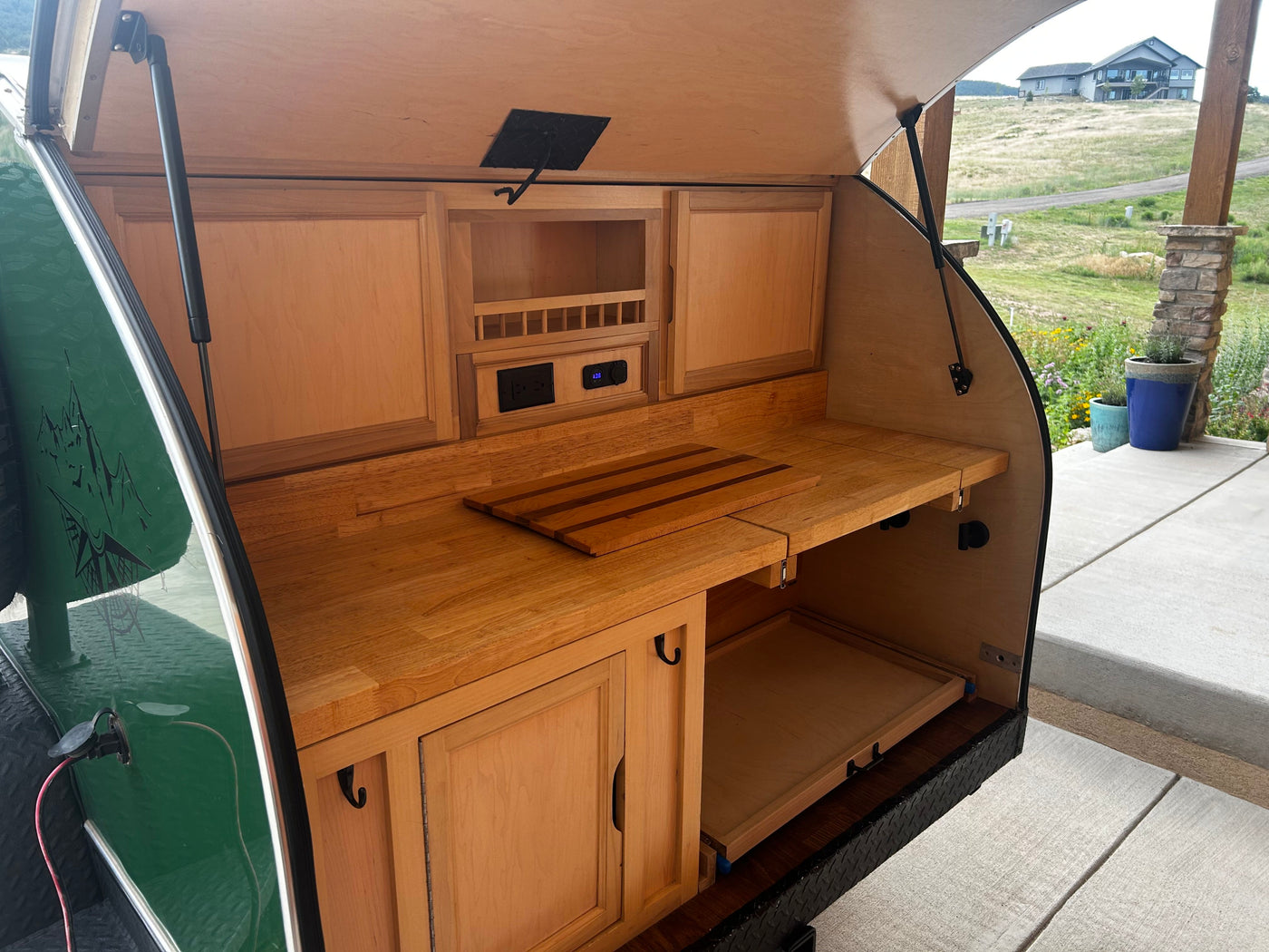 Open wooden outdoor kitchen in a teardrop trailer, with a countertop, cabinets, and power outlets. Great for RV rental. — photo 5