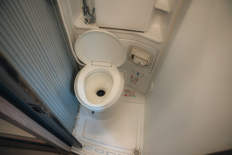 This RV rental's compact bathroom features a white toilet, shower base with drain, and slatted retractable door.