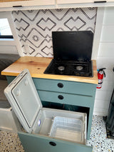 Compact RV rental kitchen featuring a two-burner stove, pull-out fridge, and fire extinguisher, set against stylish backsplash.