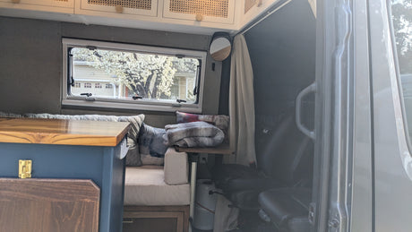 Cozy RV rental interior with a window view of a blossoming tree, comfy seating, wooden finishes, and a small mirror.