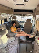 Enjoying an RV rental: Woman reading inside her campervan, legs up. A serene travel moment.