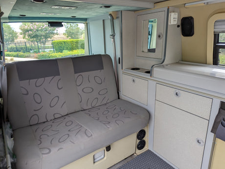 RV rental interior featuring a patterned bench seat, compact kitchenette, and storage. Ready for your next adventure!