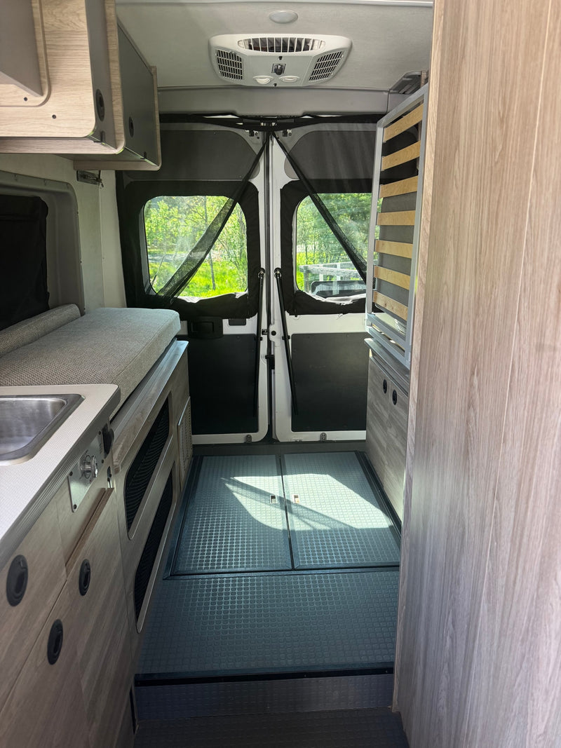 Interior of an RV rental: a compact living space with a sink, cushioned bed, and screened rear doors open to nature. — photo 8