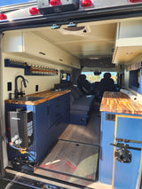 Inside this modern RV rental: blue cabinets, wooden counter kitchen, cozy bed, and efficient Gasland water heater for road trips.
