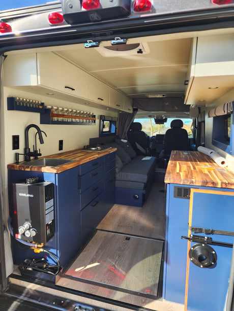 Inside this modern RV rental: blue cabinets, wooden counter kitchen, cozy bed, and efficient Gasland water heater for road trips.
