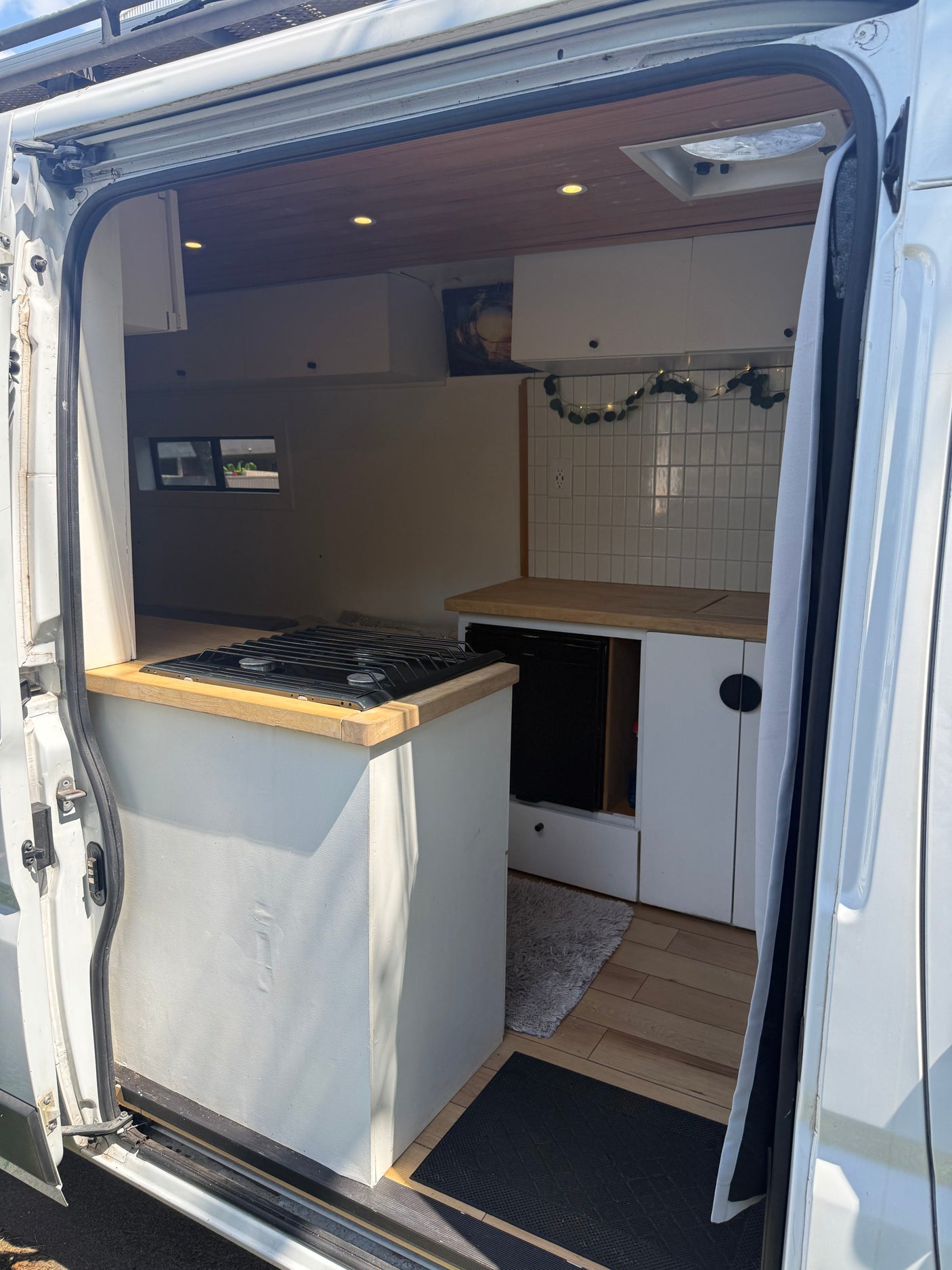 View into an rv rental camper van's modern kitchen with stove & cabinets, plus a bed platform, from the open side door.