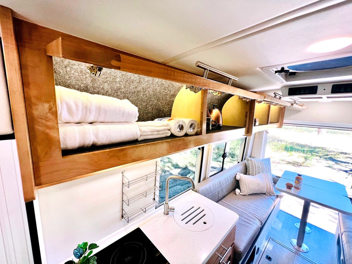 Step inside this RV rental! Features include practical overhead storage, a compact kitchenette, and a comfy dining/seating area. — photo 11