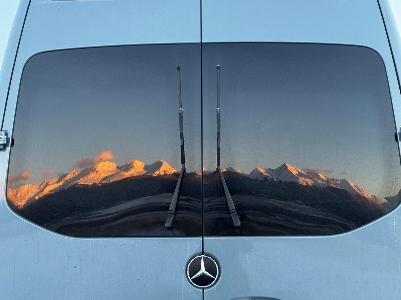 RV rental van's rear window reflects stunning golden hour mountains. Perfect for scenic travel adventures.
