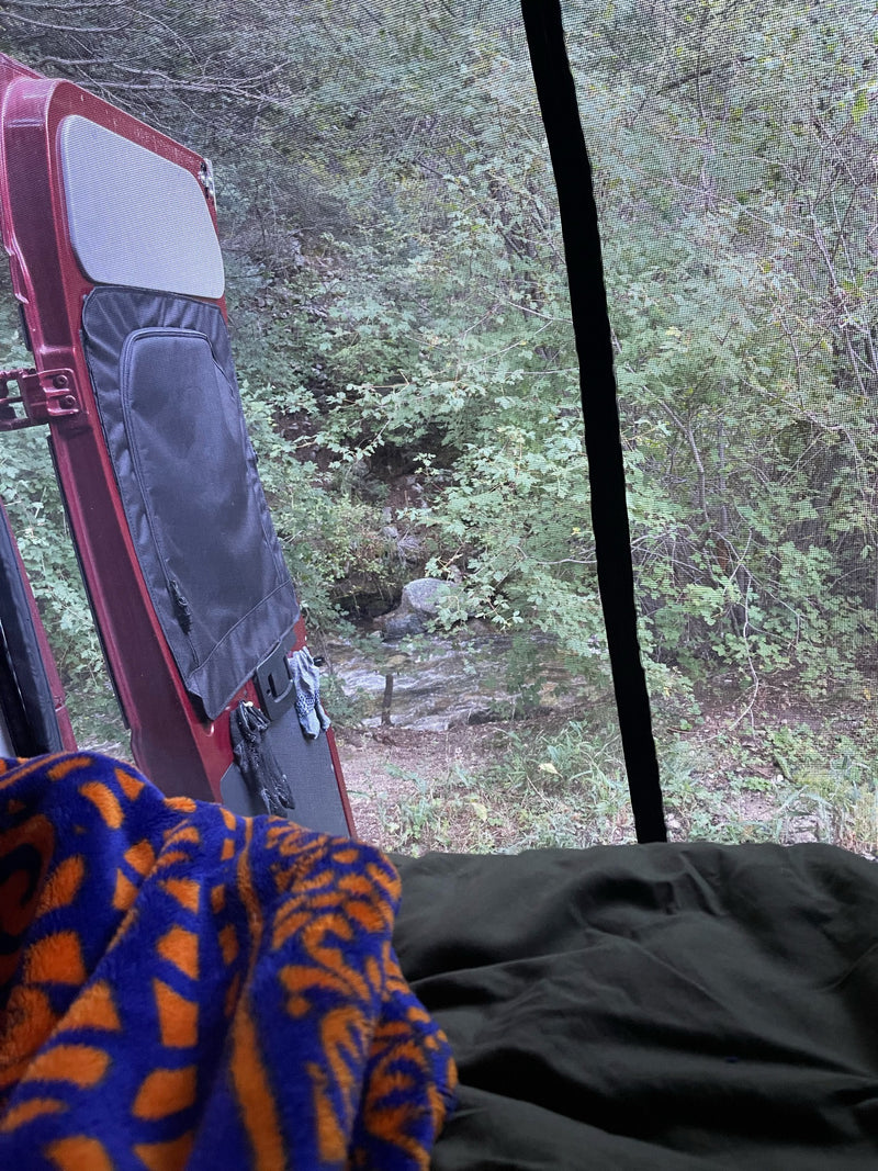 Cozy in an RV rental, viewing a lush forest and stream through an open, screened door from a comfortable bed. — photo 12
