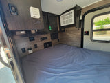 Step into this RV rental's cozy interior, featuring a comfortable bed, AC, thermostat, and essential controls.