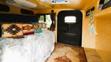 Inside this cozy RV rental: a plush bed with Southwestern pillows, soft blanket, and colorful rug. Perfect for travel comfort.