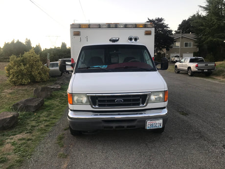 Front view of a white Ford van, a great option for an RV rental. It's parked on gravel, with homes and trees in the background.
