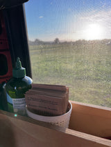 RV rental morning view: Sun through a screen, with a green bottle and 'Streetlevel' drink packets on a wooden shelf.