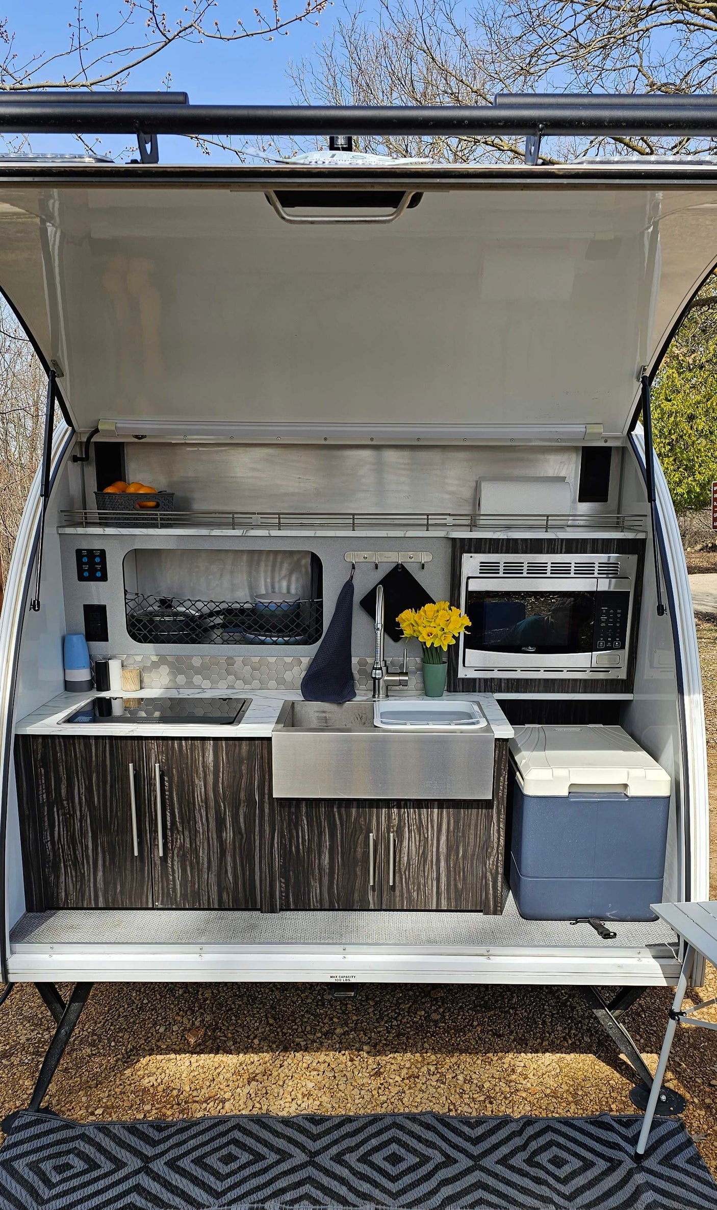 Compact RV rental outdoor kitchen setup with sink, stove, microwave, and cooler, perfect for camping.