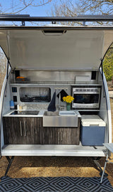 Compact RV rental outdoor kitchen setup with sink, stove, microwave, and cooler, perfect for camping.