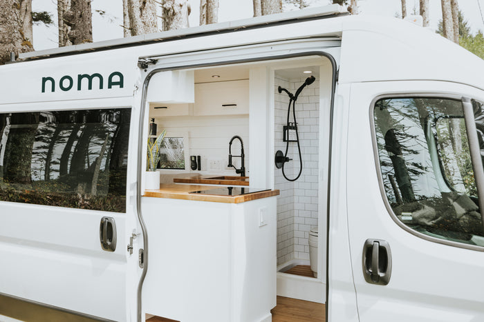 Stylish white rv rental with open side door revealing a modern interior: kitchen, wood counters, and a compact shower.