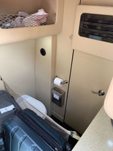 Compact RV rental interior shows a small toilet, storage nets with luggage, and built-in cabinets, optimizing space for travel.