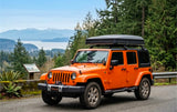 An orange Jeep Wrangler with a rooftop tent, ideal for your next RV rental adventure, overlooks a scenic lake and mountains.