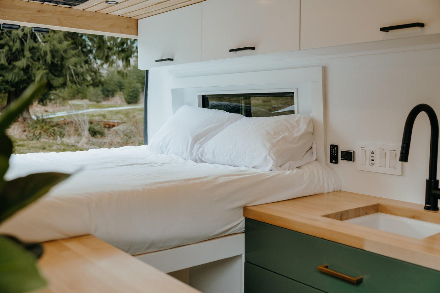 Comfortable rv rental interior featuring a neatly made bed, modern kitchen area with sink, and overhead storage cabinets. — photo 14