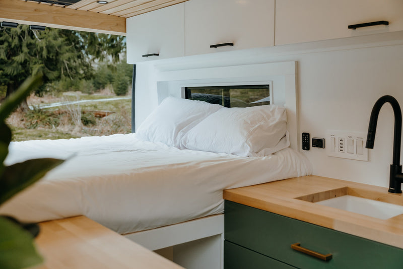 Comfortable rv rental interior featuring a neatly made bed, modern kitchen area with sink, and overhead storage cabinets. — photo 14