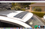 White RV rental with a flexible solar panel installed on its curved roof and roof racks, displayed in a QuickTime Player window.