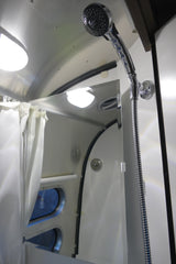 RV rental shower features a modern chrome showerhead, white curtains, and mirror reflecting bright interior lights.
