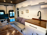 Cozy RV rental interior featuring shiplap walls, wood ceiling, kitchen with sink, bench seating, and an adjustable table.