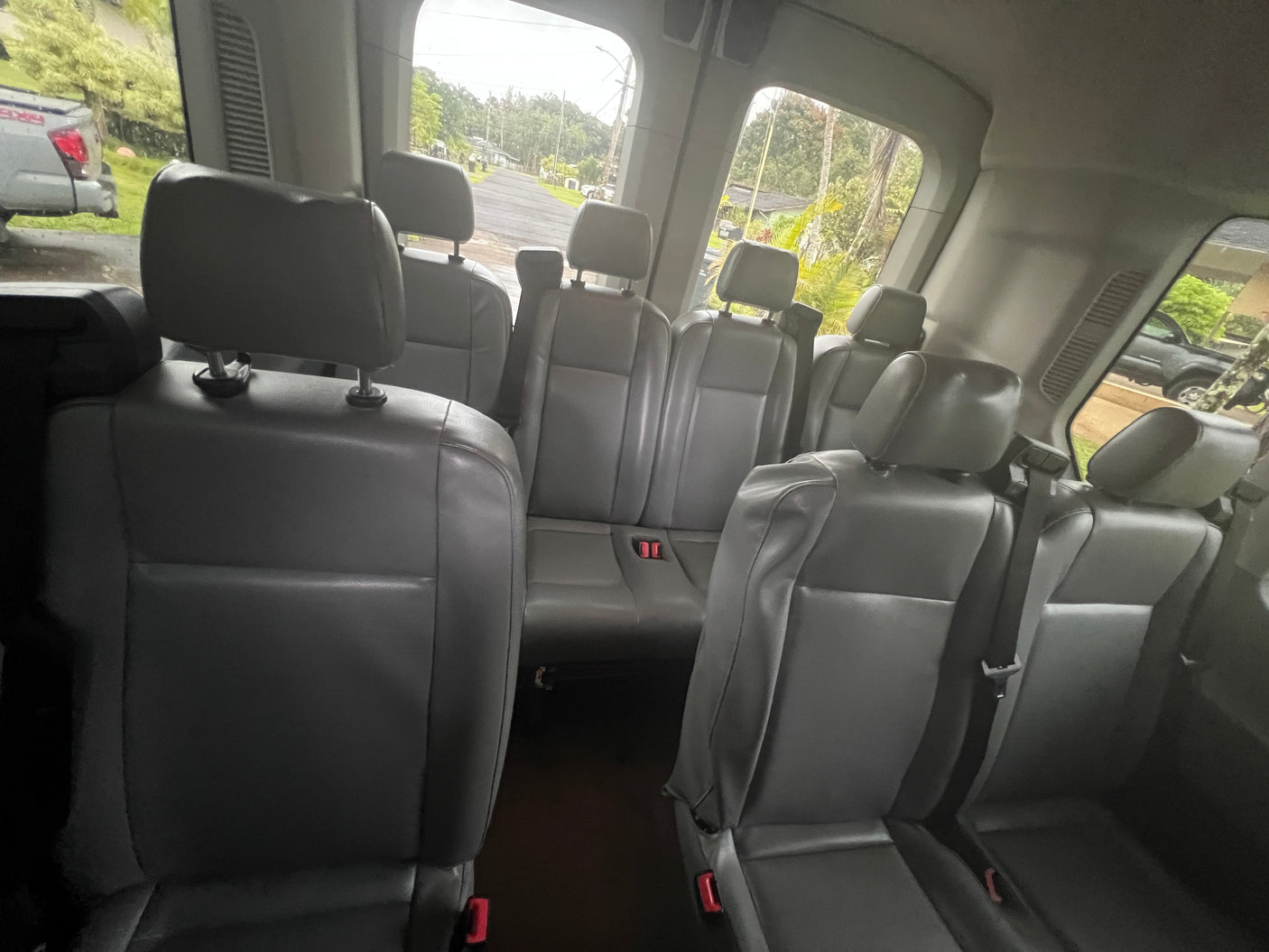 Spacious grey interior of an RV rental passenger van, showing rows of seats. Outside, a road and trees are visible.