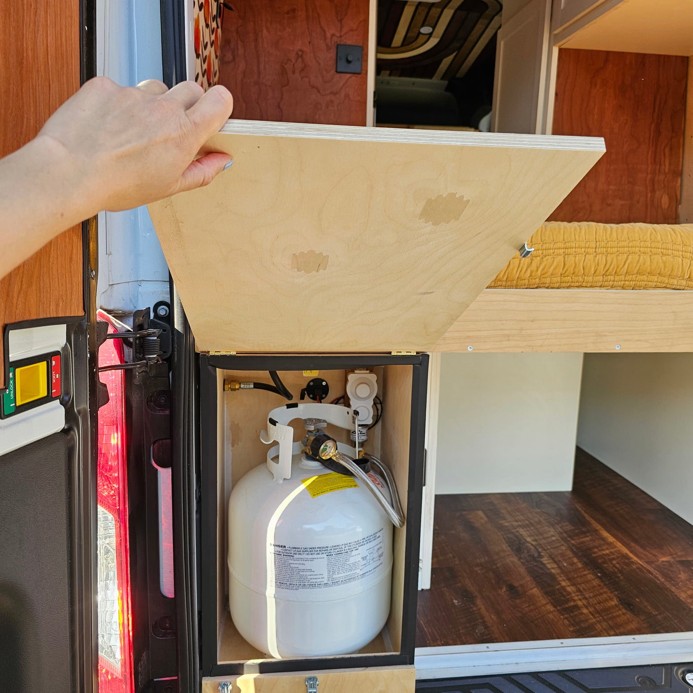 Hand opening RV rental cabinet revealing a neatly installed propane tank storage for camping convenience in a camper van.