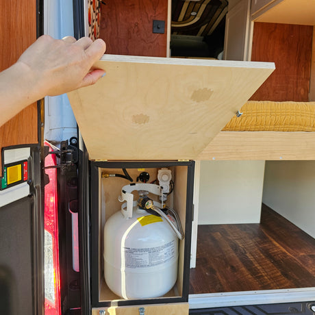 Hand opening RV rental cabinet revealing a neatly installed propane tank storage for camping convenience in a camper van.
