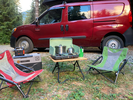 Red RV rental van with full outdoor camping setup: portable stove, table, cooler, and chairs. Perfect for van life adventures.