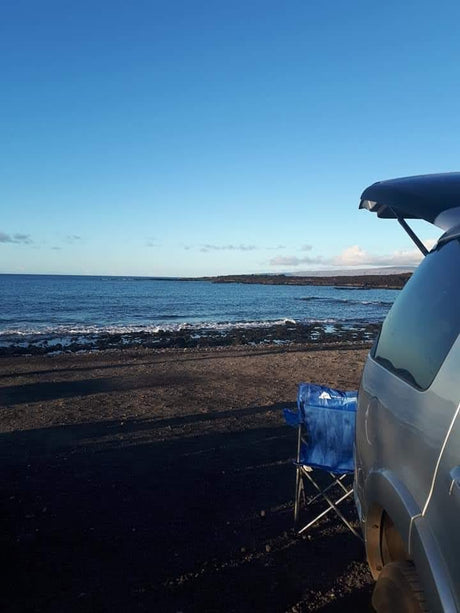 Coastal RV rental view: blue chair on dark shore, ocean waves & clear skies. Perfect beach relaxation.