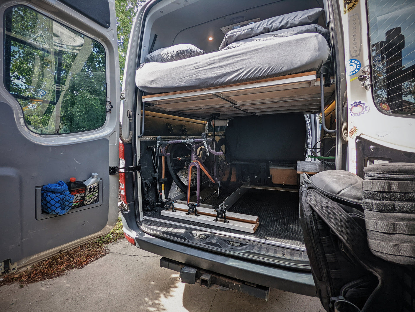 Spacious rv rental camper van interior showing a raised bed, under-bed bike storage, and practical rear door organization.