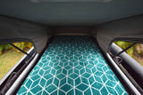 Cozy RV rental pop-top bed with geometric teal blanket & nature views for a comfortable night.