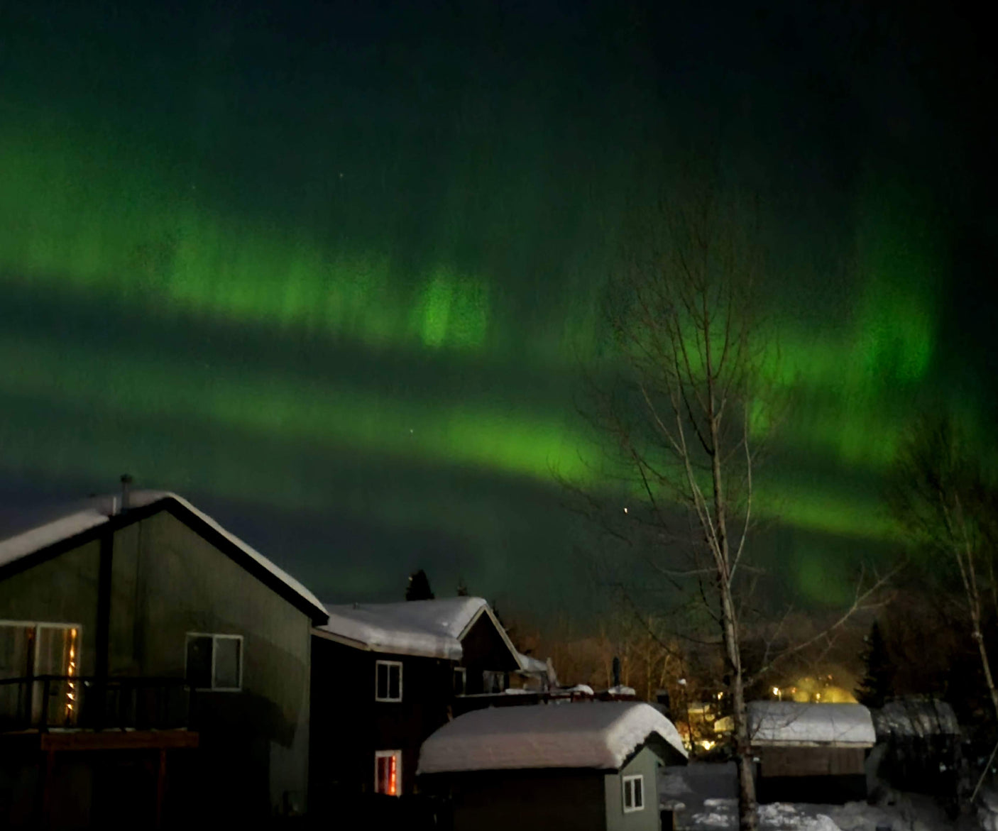 Green Aurora Borealis over snow-covered houses, a stunning night sky view perfect for your next rv rental adventure.