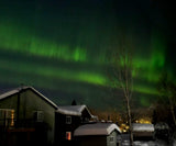 Green Aurora Borealis over snow-covered houses, a stunning night sky view perfect for your next rv rental adventure.
