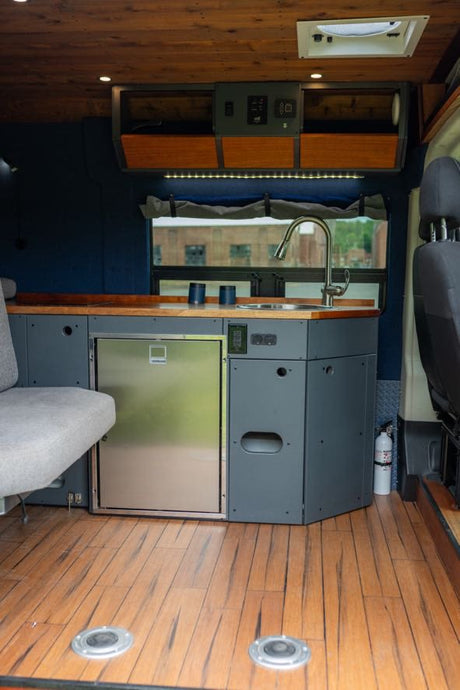 RV rental interior: compact kitchen with sink, stainless fridge, wood counters, and a light grey bench seat.