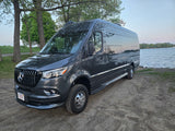 Dark gray Mercedes Sprinter rv rental camper van parked by a scenic lake under clear skies, surrounded by trees.