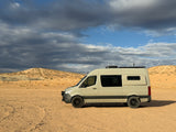 Adventure-ready RV rental parked in a vast desert landscape under dramatic skies, perfect for off-road travel and camping.