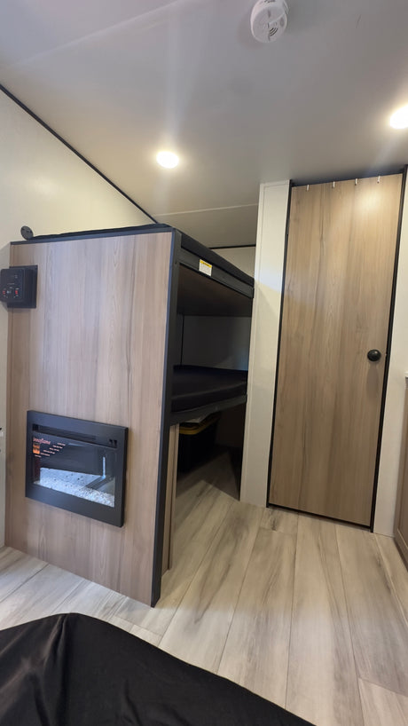 This RV rental interior features compact bunk beds, an electric fireplace, and a light wood door, all designed for functional travel.