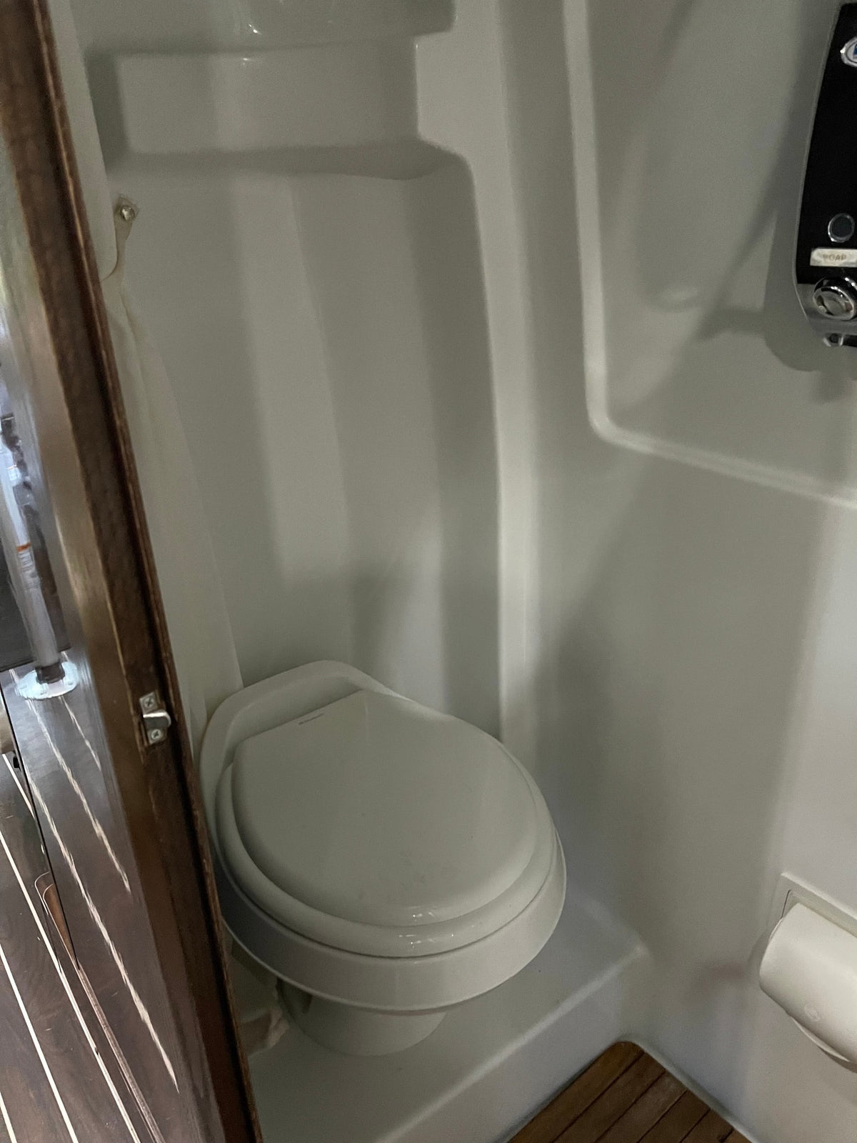 Compact RV rental bathroom with a white toilet inside a molded shower stall. Includes toilet paper holder & shower controls. — photo 15